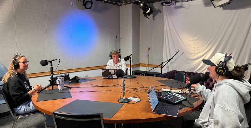 Cooper Hillman, Anne Borberg and Delaney Murphy sit around a large table in a Studio at Wildcat 91.9