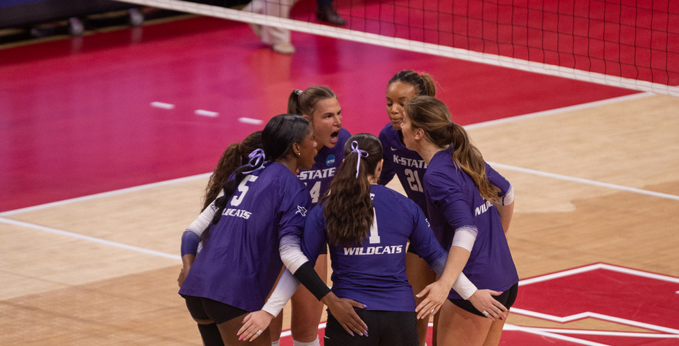 K-State volleyball players huddle together at midcourt.
