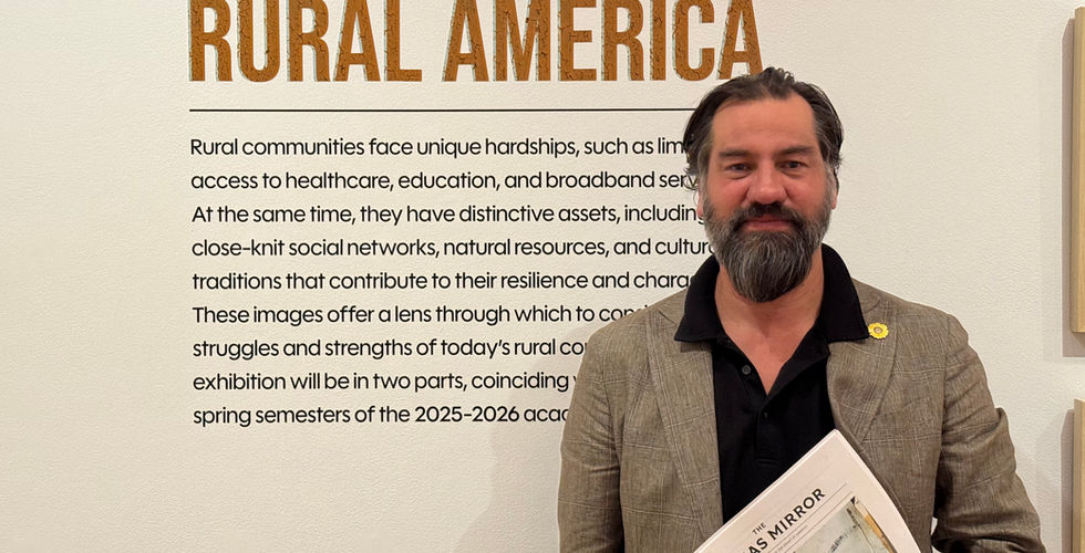Jeremiah Ariaz standing in front of a "Rural America" sign in his exhibit