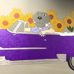 A mural featuring Willie the Wildcat driving a vibrant purple vintage convertible, surrounded by an array of bright sunflowers.