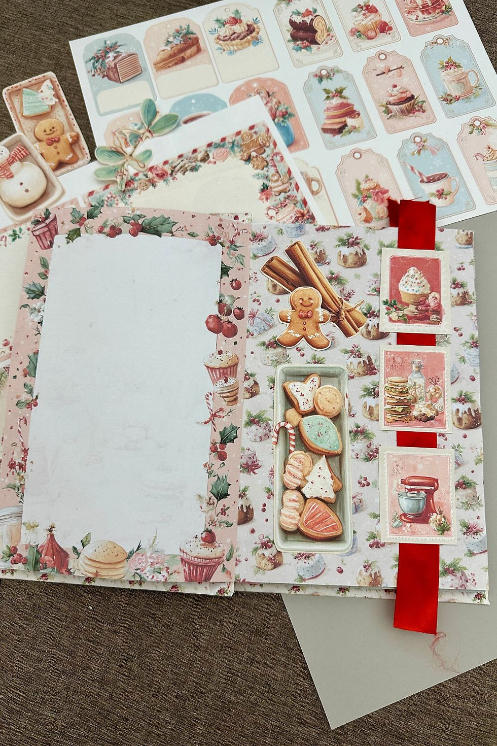 Christmas junk journal open to a page with baking themed fussy cuts arranged on top of a red ribbon.