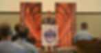 Speaker at CCLE conference standing at a podium in front of banners