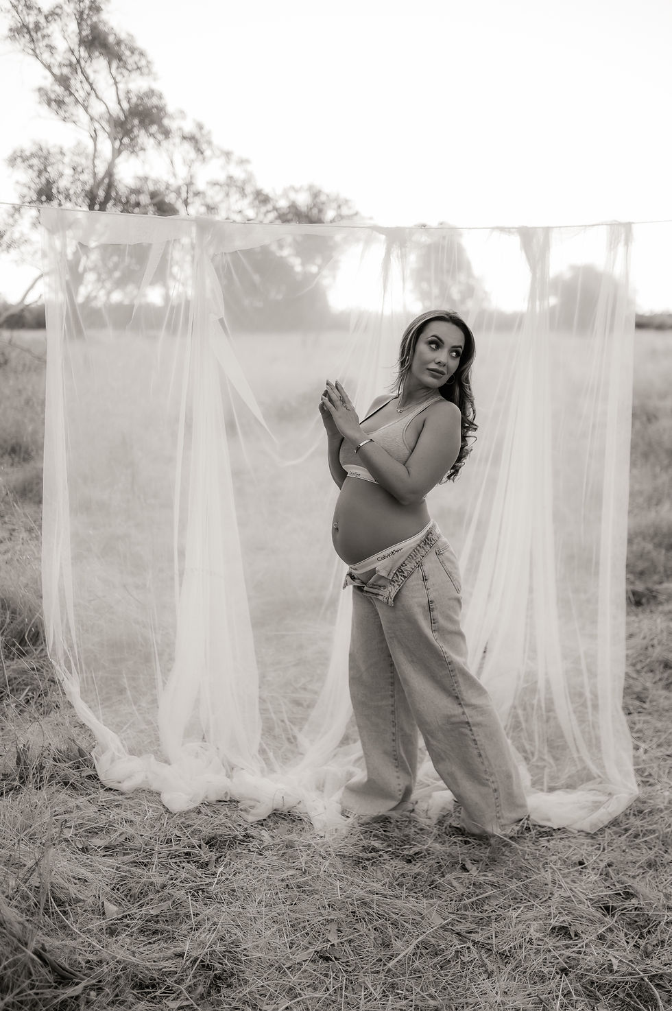 Pregnant mother in black and white, in a field wearing jeans and a crop top