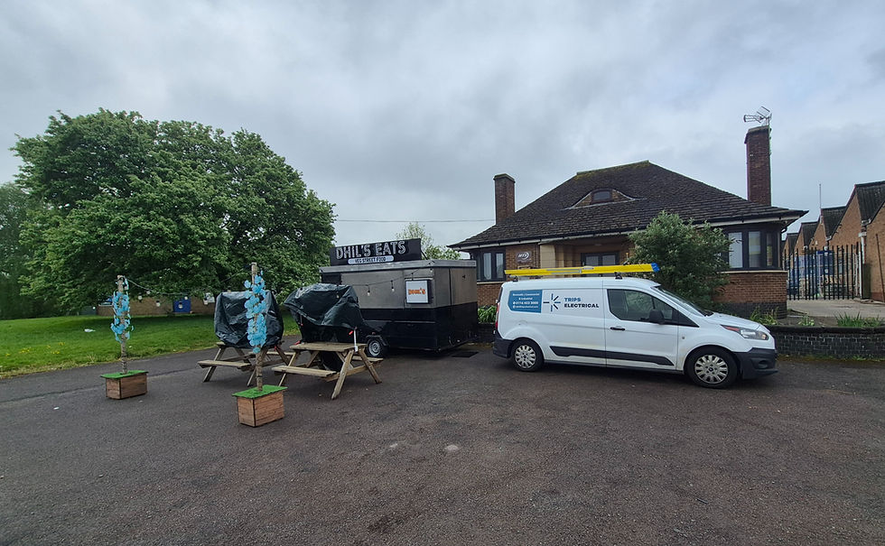 Midlands food stand 'Rub & Sides' with picnic tables and van next to a Trips Electrical van.