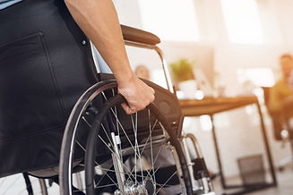 A disabled man is sitting in a wheelchair. He holds his hands on the wheel. Nearby are his...ues.jpg