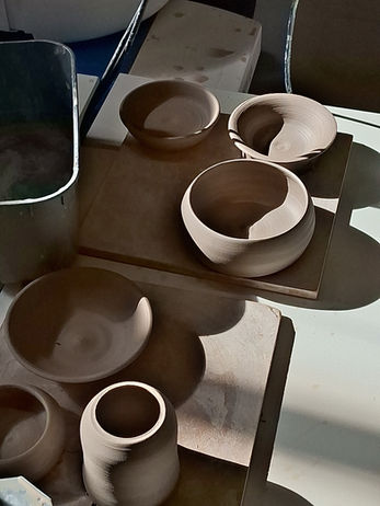 Gedroogde kleipotjes op houten planken klaar voor de biscuitstook in de keramiekoven