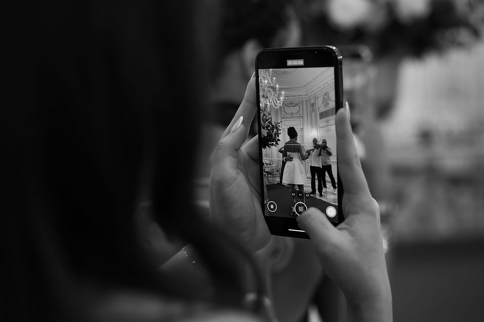 Imagem em preto e branco de um smartphone capturando uma cena de um evento formal, apresentando uma mulher e um fotógrafo.