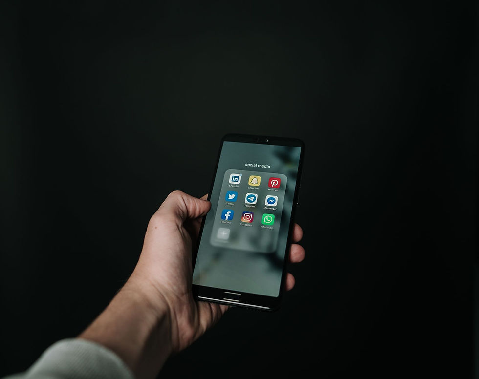 Close-up de uma mão segurando um smartphone exibindo vários ícones de aplicativos de redes sociais em um fundo escuro.