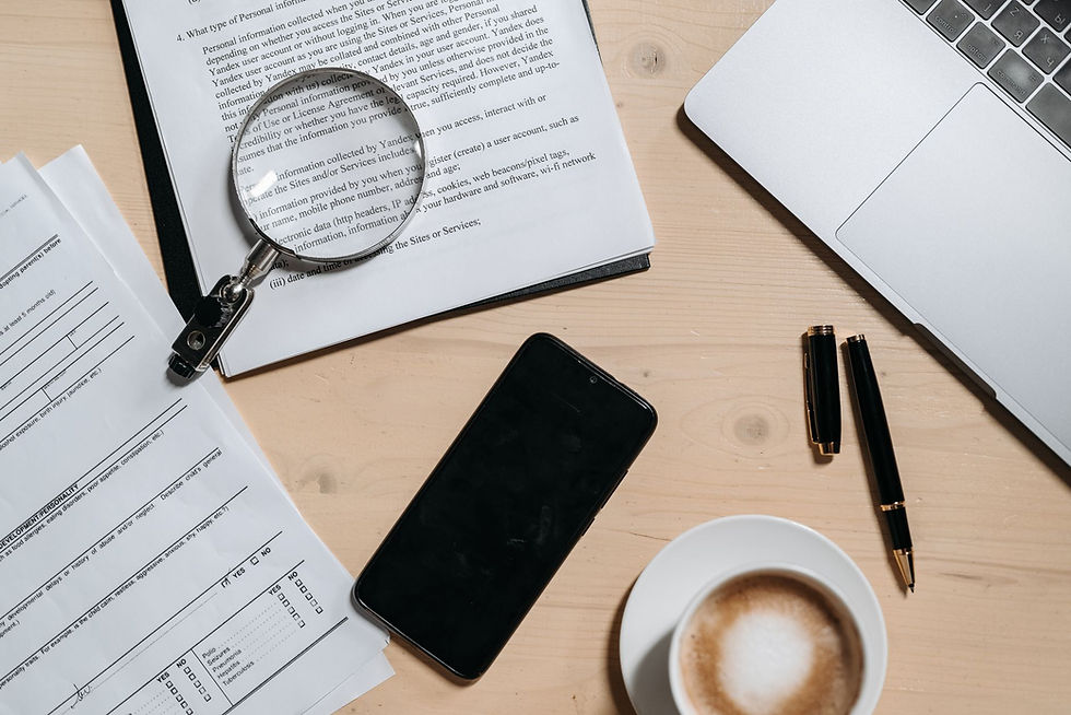 Visão superior de documentos, laptop, café e lupa sobre uma mesa de escritório.