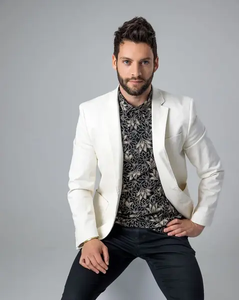 Man in a white blazer seated on a gray backdrop