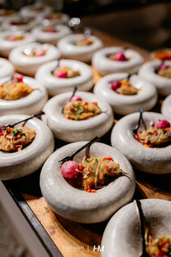 תקריב על עמדת הגשה מעוצבת באירוע Desert Night ✦ TLV Stock Exchange. שורות של קעריות קרמיקה לבנות בעלות צורה מעוגלת וייחודית מכילות מנות גורמה אישיות המעוטרות בפרחי מאכל וצמחי תבלין, המוגשות על משטח עץ טבעי. הפקה: חגי מגידו – HM Productions.