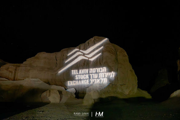הקרנת לוגו עוצמתית בלבן על גבי צוק סלע טבעי וגדול בחשיכה. הכיתוב המוקרן כולל את לוגו "הבורסה לניירות ערך תל אביב" בעברית ובאנגלית: "TEL AVIV STOCK EXCHANGE". המיצב מייצג את החיבור הקונספטואלי בין המוסד התל אביבי לבין האווירה המדברית של האירוע. הפקה: חגי מגידו – HM Productions.