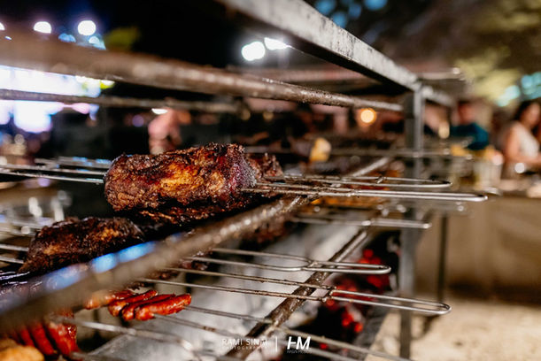 צילום אמנותי בשחור-לבן הלוכד זמרת ברגע של שיא רגשי על הבמה באירוע Desert Night ✦ TLV Stock Exchange. היא עומדת בפריסת ידיים רחבה מול הקהל, כשמאחוריה תאורה אחורית (Backlight) עוצמתית המייצרת סביבה הילה של אור וערפל דרמטי. הקהל נראה בצלליות בחזית התמונה, מה שמעצים את תחושת האינטימיות והחיבור למופע. הפקה: חגי מגידו – HM Productions.