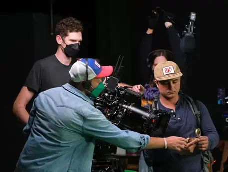Director helps an actor in front of a film camera.