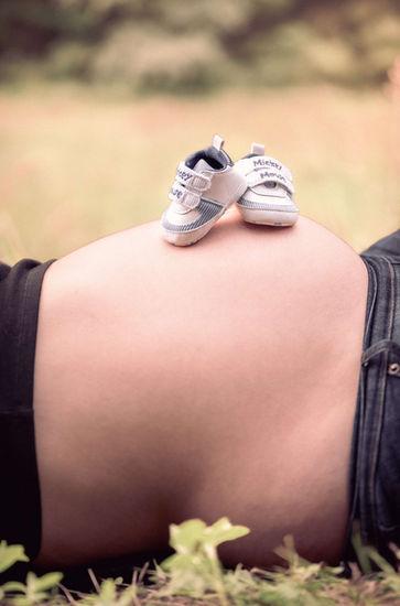 Schwangere Frau mit Babyfüßlingen auf dem Bauch, Babybauchfotografie, im Gras liegend.
