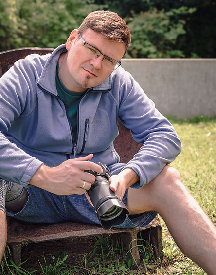 Mann mit Brille hält Kamera, im Garten sitzend. Fotograf aus Jena – Bastiontour-Fotoshoot.