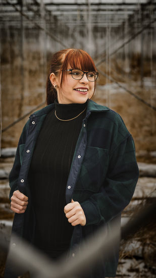 Junge Frau mit Brille und Jacke lächelt, im Hintergrund Gestell, Portraitfotografie Jena.