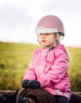 Kleines Mädchen mit Helm und Jacke sitzt auf einem Pferd. Bastiontour-Fotoshoot.