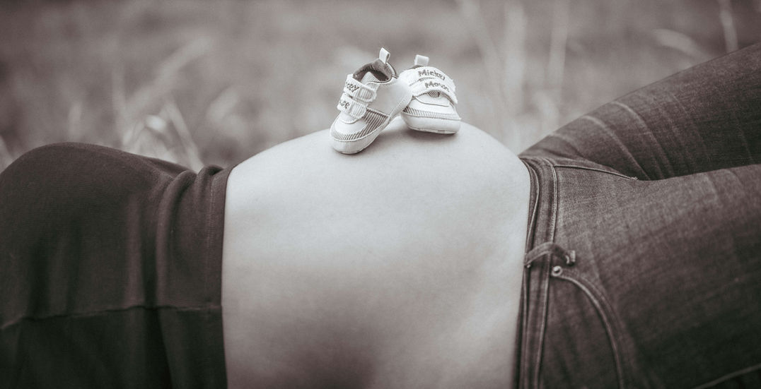 Schwangere Frau mit Babyschuhen auf dem Bauch, Babybauchfotografie und im Freien.