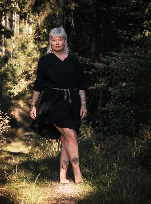 Woman in black dress posing, tattoos visible, in a forest background, Bastiontour-Fotoshoot.