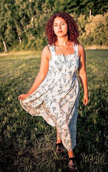 Eine junge Frau im Sommerkleid steht auf einer Wiese. Portraitfotografie.