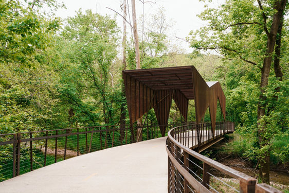 this image shows an edgy covered bridge made of corten steel through lush woods