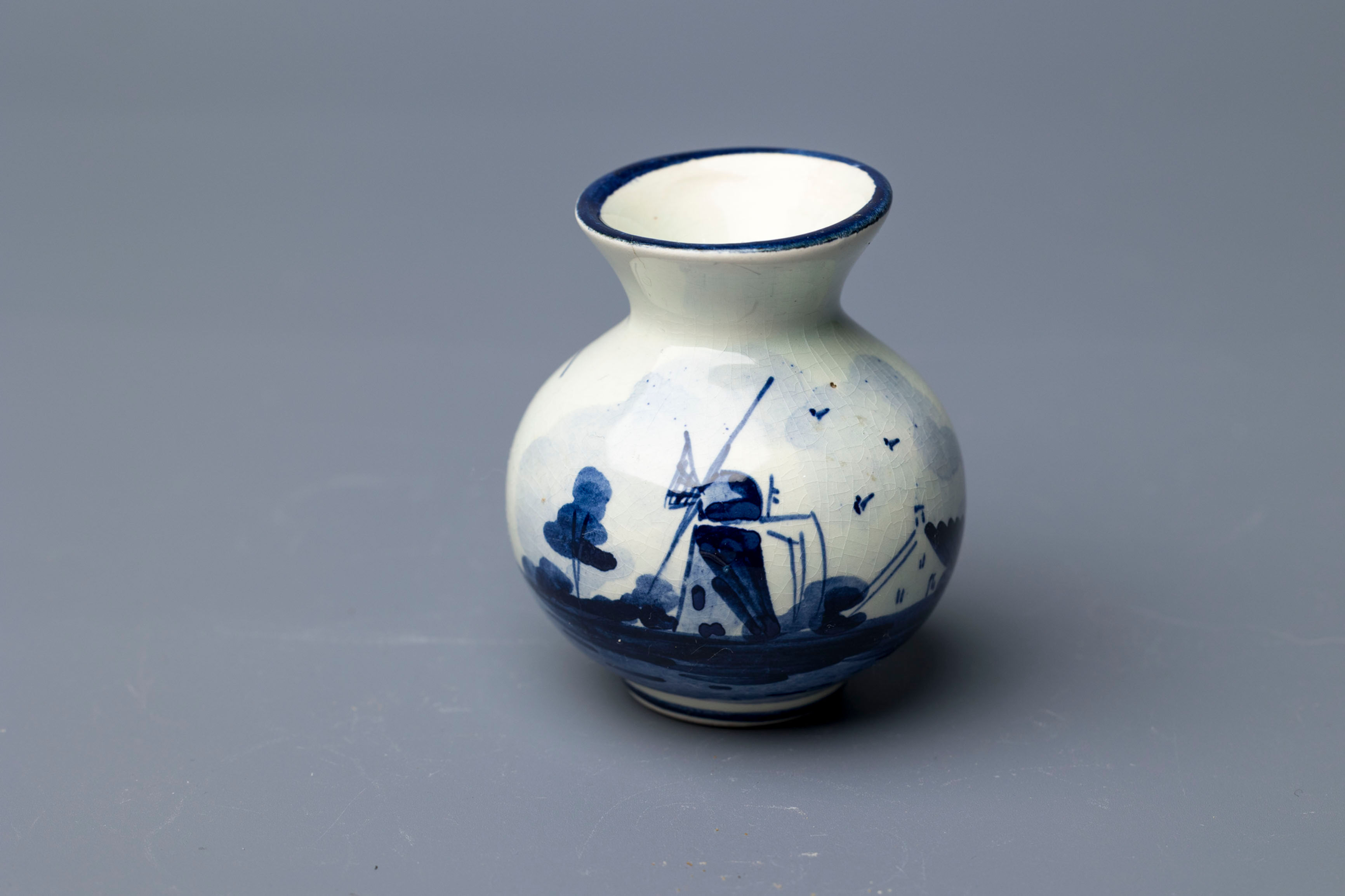 This is a small bulbous vase featuring a hand-painted traditional Dutch windmill scene, rendered in classic cobalt blue under