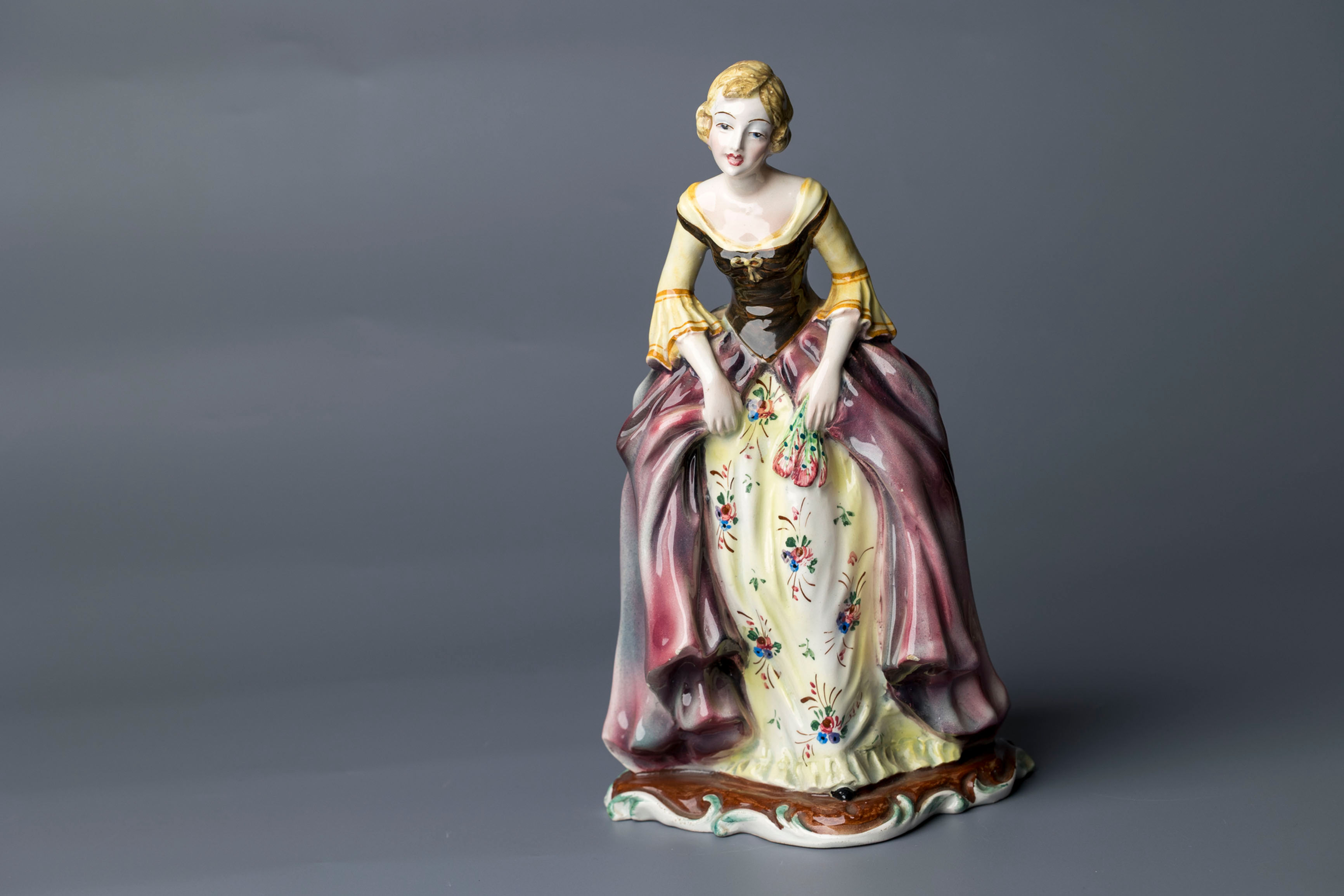 A striking mid-century continental porcelain figurine, this elegant lady stands poised in a floral gown of rich burgundy and