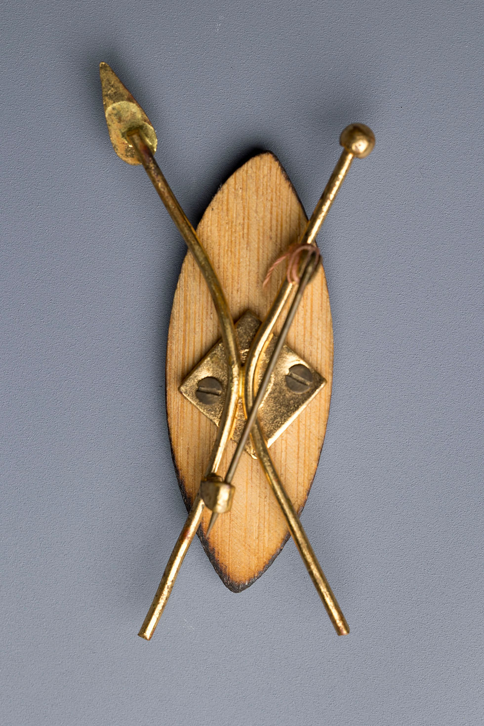 A vintage painted wooden souvenir brooch in the form of a Zulu-style shield, featuring a stylized figure and mounted