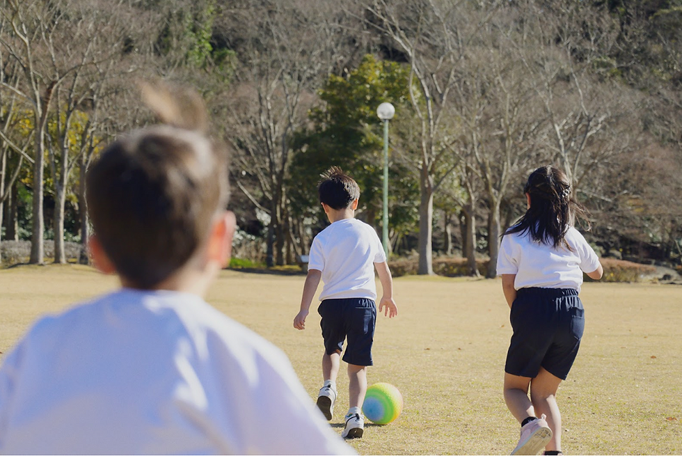 体操服を着た子供3人が公園でサッカーをして走っている