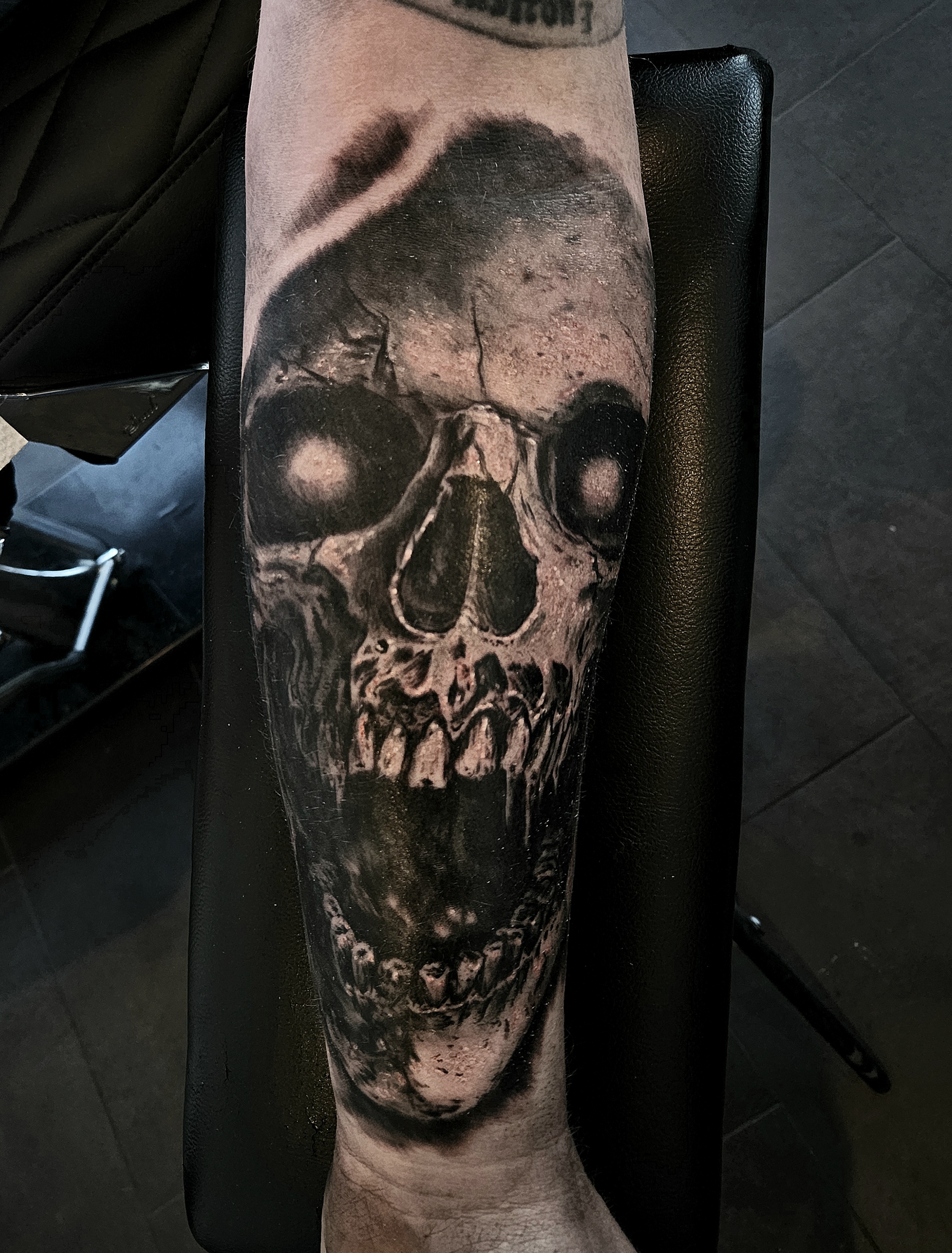 Black and grey open-mouth skull forearm tattoo