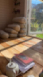 Sunlight streams into yoga studio, illuminating bolsters, book, and teapot