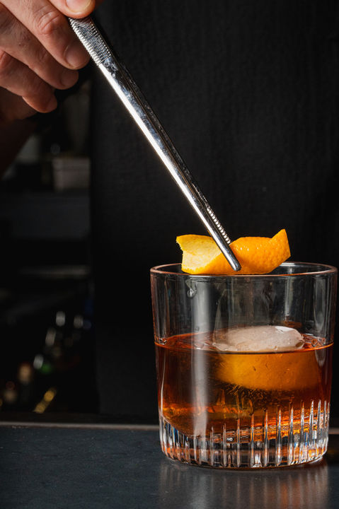 Bartender garnishing Old Fashioned cocktail with orange peel, close up shot.