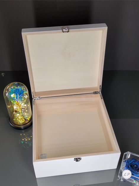 An open, empty wooden box with a white exterior sits on a reflective surface. Next to it are a glass dome containing a gold-l