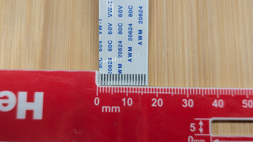 Thumbnail: A flat white ribbon cable with blue text lies on a wooden surface, next to a red ruler showing millimeter measurements, with
