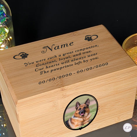 A wooden pet memorial box with an engraved message, paw prints, and blank name and date fields. A photo of a German Shepherd