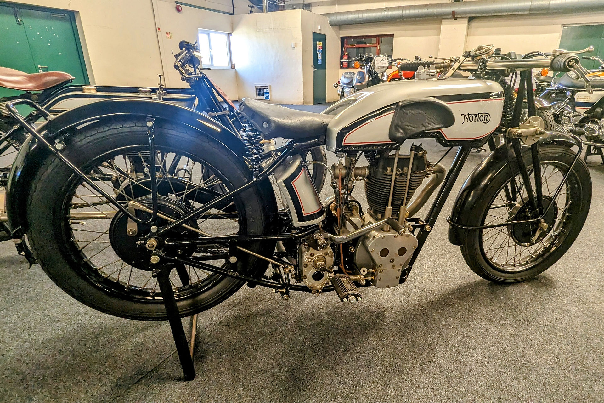 Vintage Norton motorcycle on display in an indoor showroom. Black and silver with visible engine details. Bright, well-lit setting.