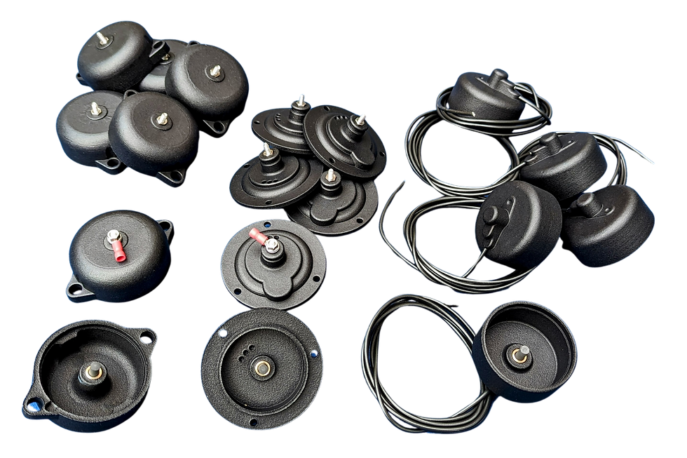 Black circular plastic magneto points caps with metal centres and coiled wires, some have red connectors, arranged on a black background.