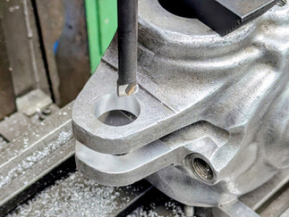 A close-up of a metal milling machine operating on a silvery engine part in a workshop.