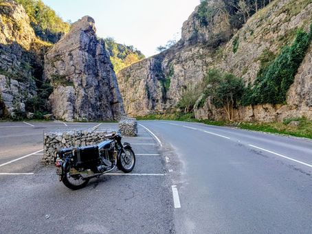 Vintage Norton ES2 motorcycle parked on an empty mountain road between steep rocky cliffs in Cheddar Gorge, with PHA 320 plate and sunny green slopes.