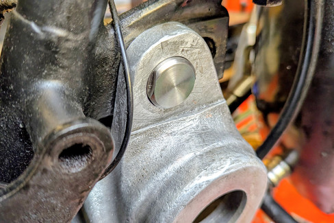 Close-up of a silver metal bolt on a Norton motorcycle gearbox with black elements and blurred background. Focus on the metallic textures.