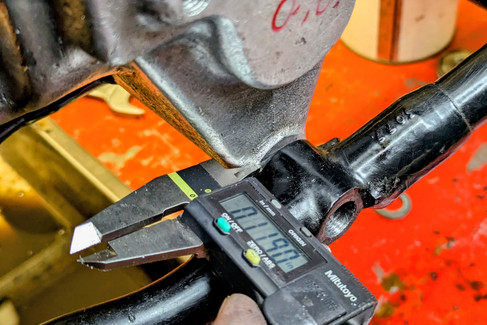 A digital caliper measures a black metal object, reading 0.1190 inches. The background is orange with blurred tools and surfaces.