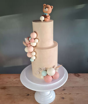 Two-tiered beige cake decorated with teddy bear and pastel balloons