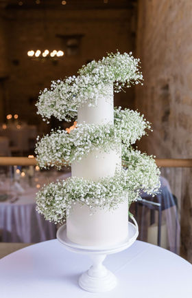 Tall tier wedding cake coated in white chocolate ganache with sharp edges and surrounded by a spiral of gypsophila flowers in Yorkshire