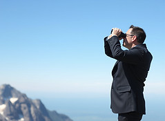 leader looking through binoculars on a mountain in a suit.jpg