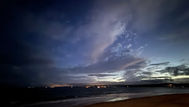 A night sky over the sea with grey clouds against a navy, pink and pale yellow sky