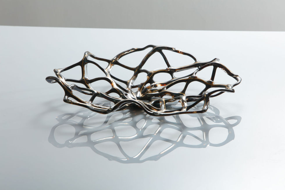 A profile view of the glass hypotrochoid design sculpture, colours are earthy tones with a gold glint, background is white.