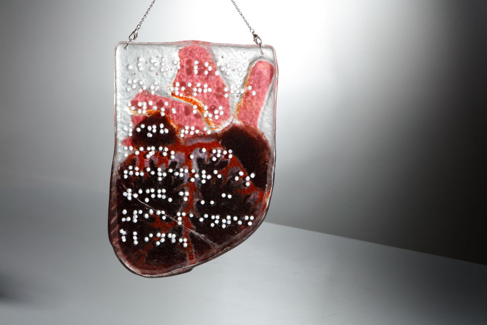 The other face of piece of clear glass with a quote in braile formed by raised white dots.