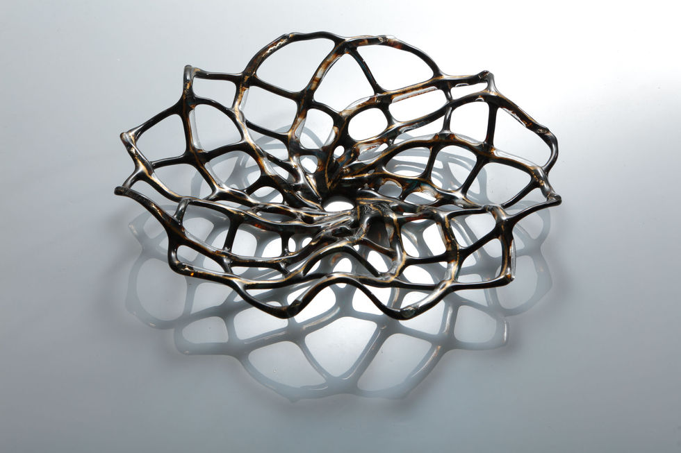 View looking down on a glass hypotrochoid design sculpture, colours are earthy tones with a gold glint, background is white.