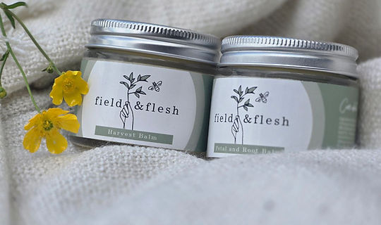Two jars of Field and Flesh balm on a soft cream rug, showcasing natural skincare products.
